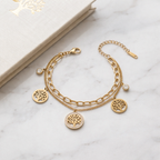 A dual-layer gold-plated chain bracelet for women featuring Tree of Life charms and clear crystal accents, displayed on a marble surface next to a white book