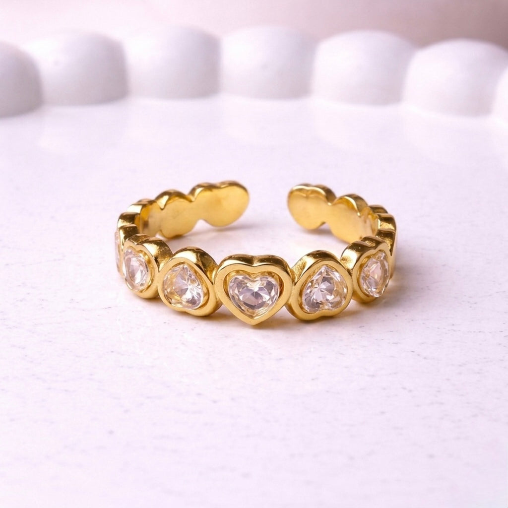 A gold plated adjustable eternity ring for women featuring a continuous row of heart-shaped white stones, displayed on a white textured surface