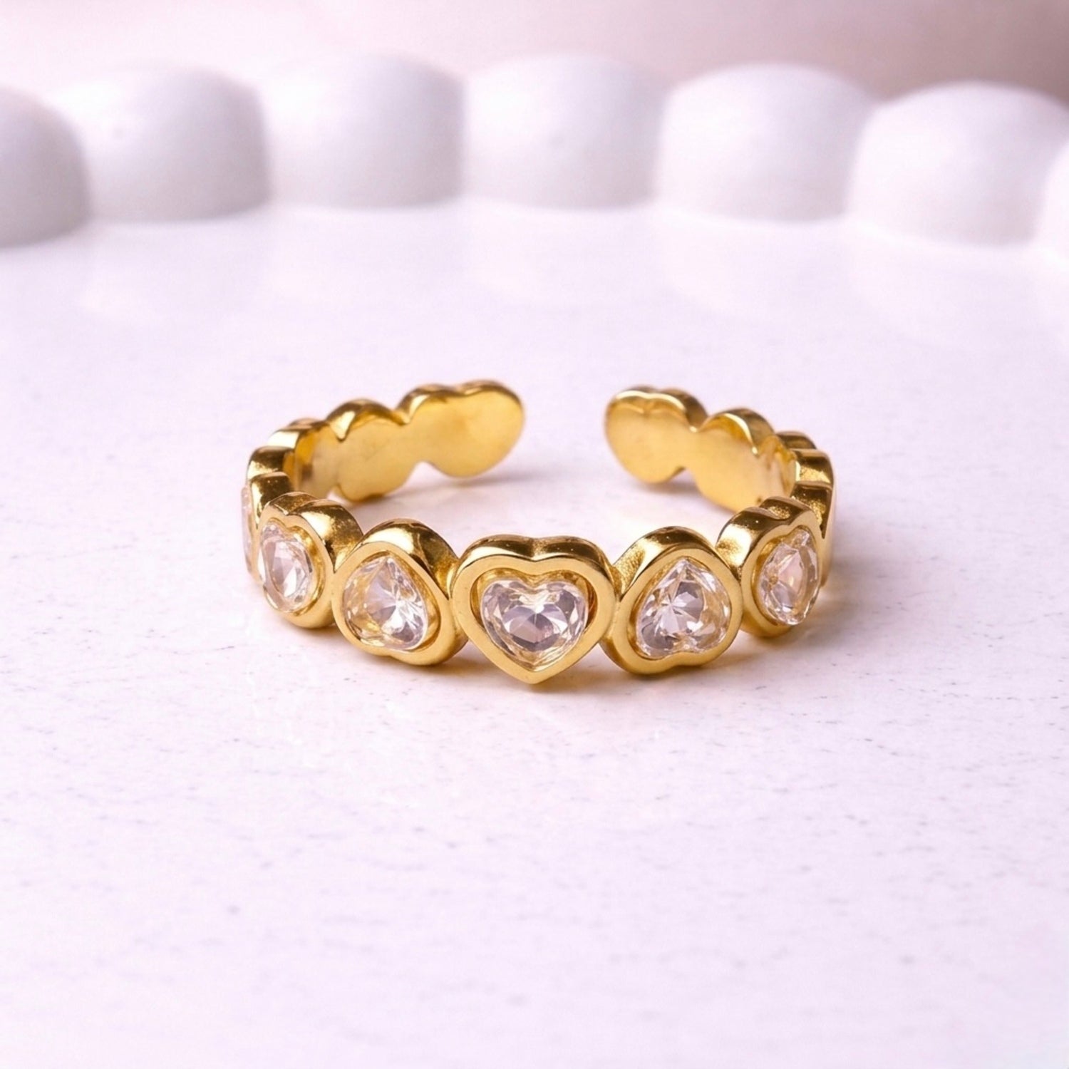 A gold plated adjustable eternity ring for women featuring a continuous row of heart-shaped white stones, displayed on a white textured surface