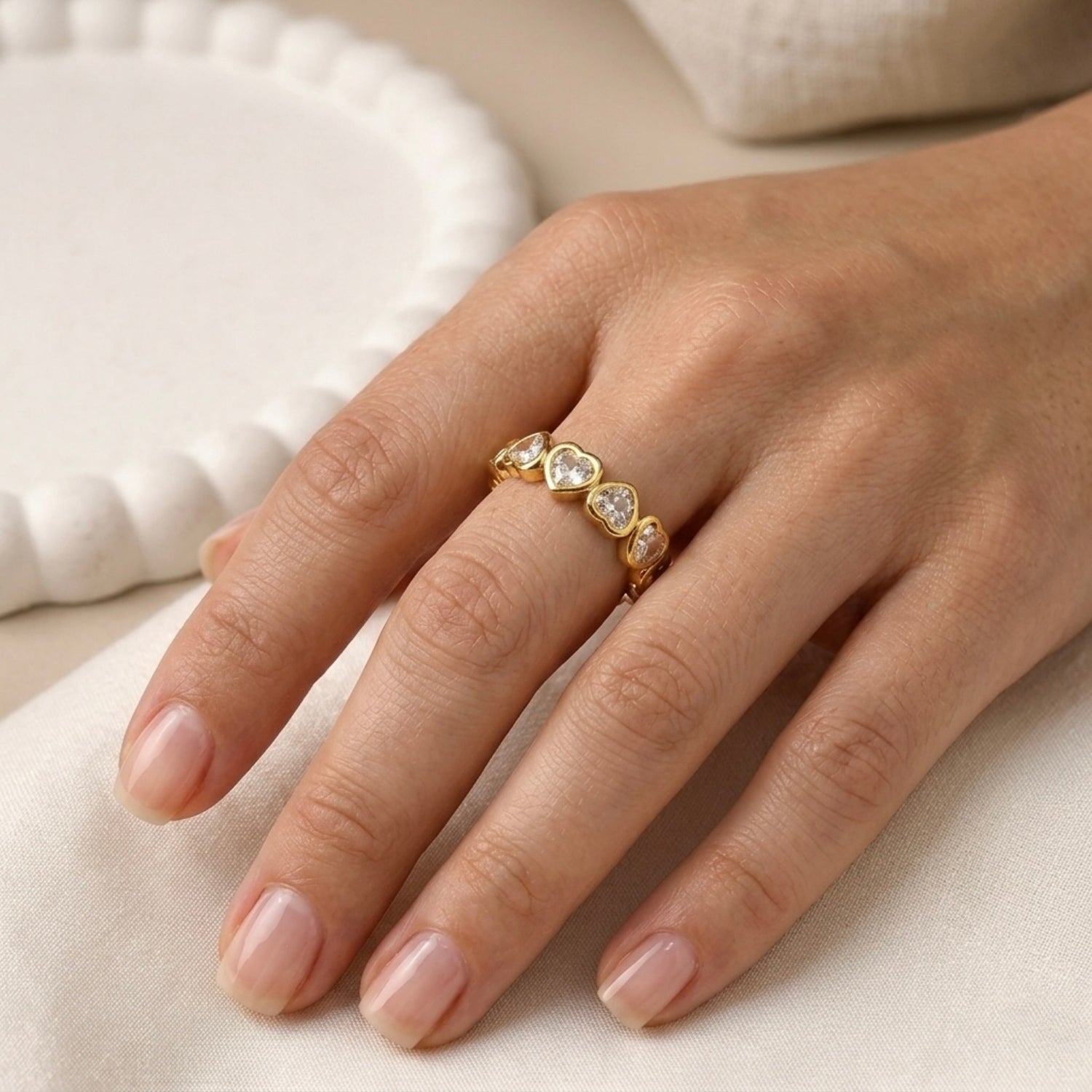 A gold plated adjustable eternity ring for women featuring a continuous row of heart-shaped white stones, displayed on a model hand