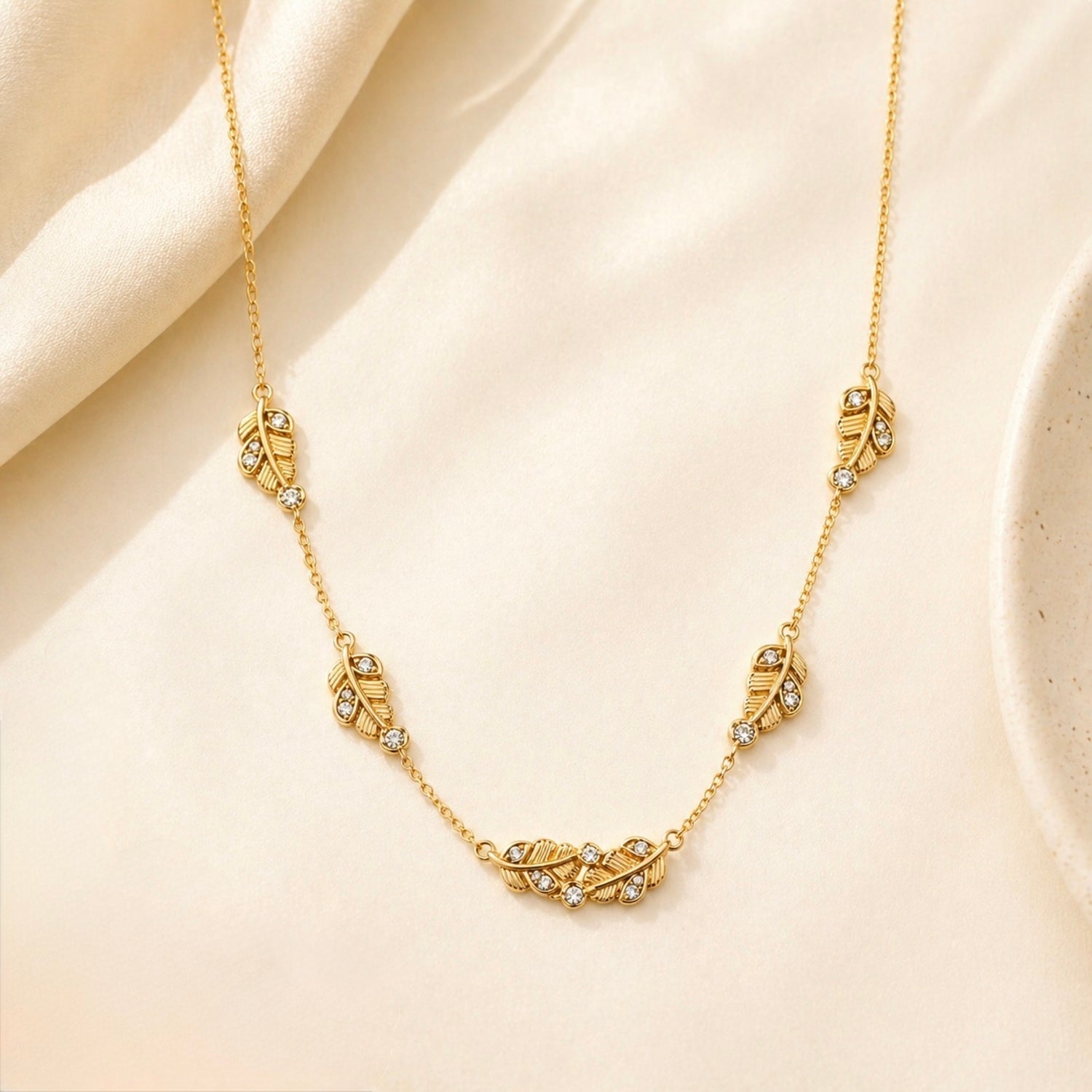 A close-view of a gold-plated stainless steel chain for women featuring five crystal-accented feather station charms