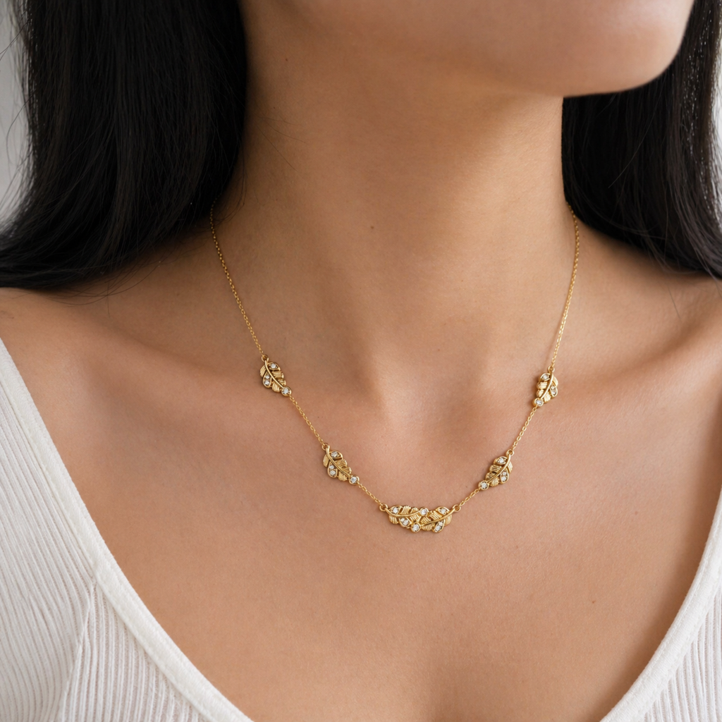 A gold-plated stainless steel chain for women featuring five crystal-accented feather station charms, shown on a model