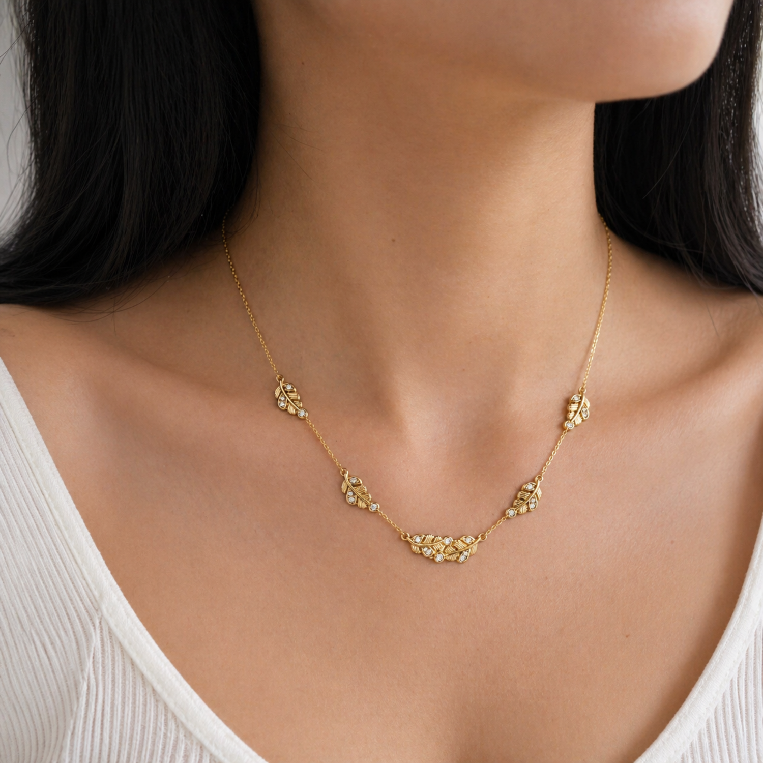 A gold-plated stainless steel chain for women featuring five crystal-accented feather station charms, shown on a model