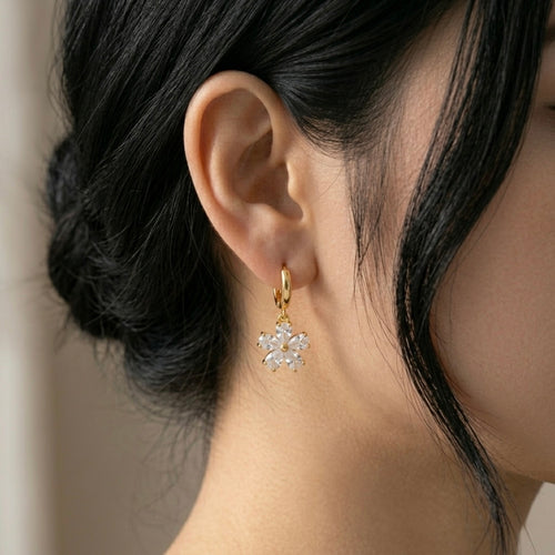 A gold-plated hoop earrings for women featuring a sparkling five-petal crystal flower drop, shown on a model