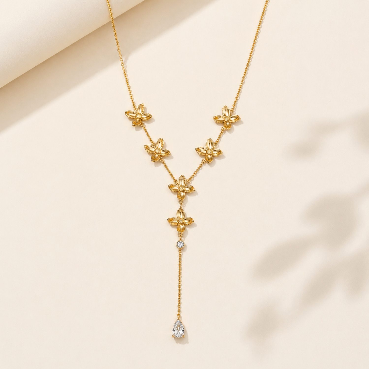 A gold-plated stainless steel chain for women in a Y-drop lariat style, featuring golden flowers and a pear-shaped crystal pendant