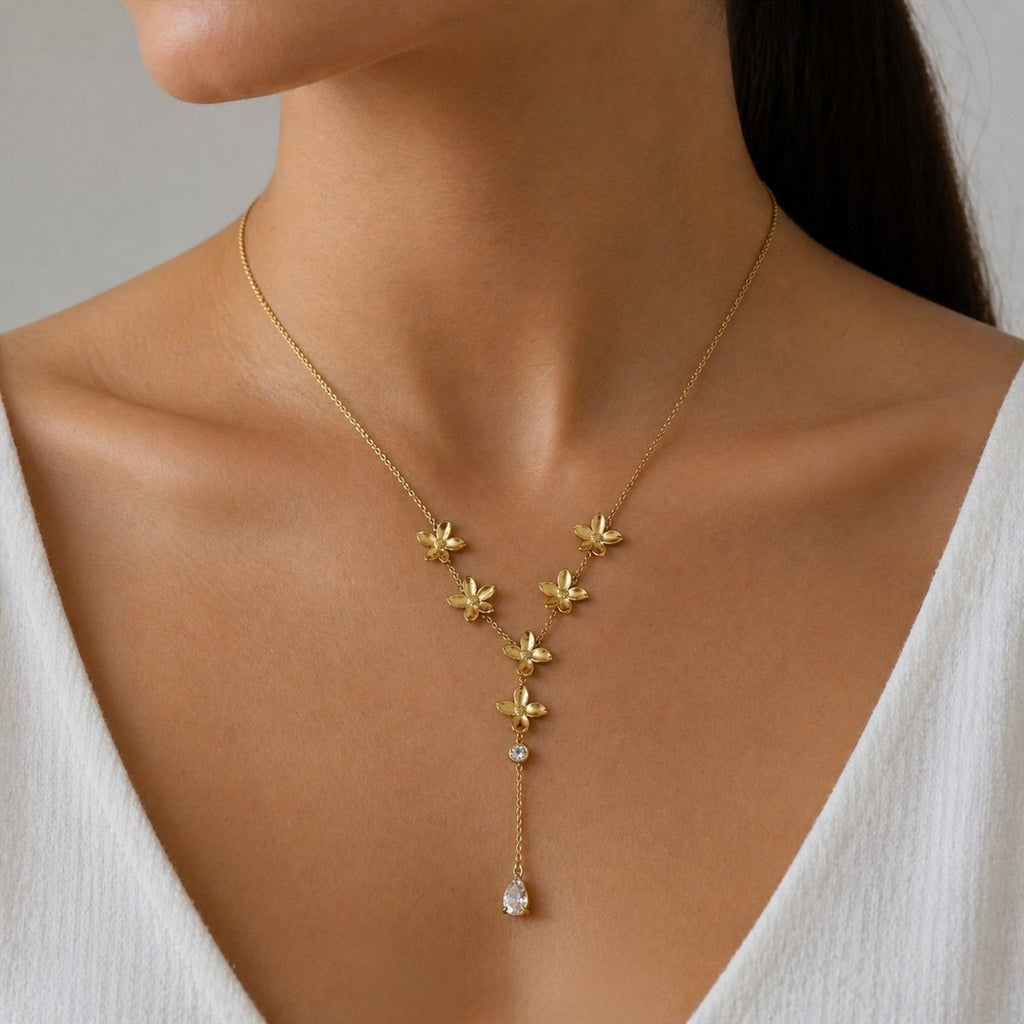 A gold-plated stainless steel chain for women in a Y-drop lariat style, featuring golden flowers and a pear-shaped crystal pendant, shown on a model
