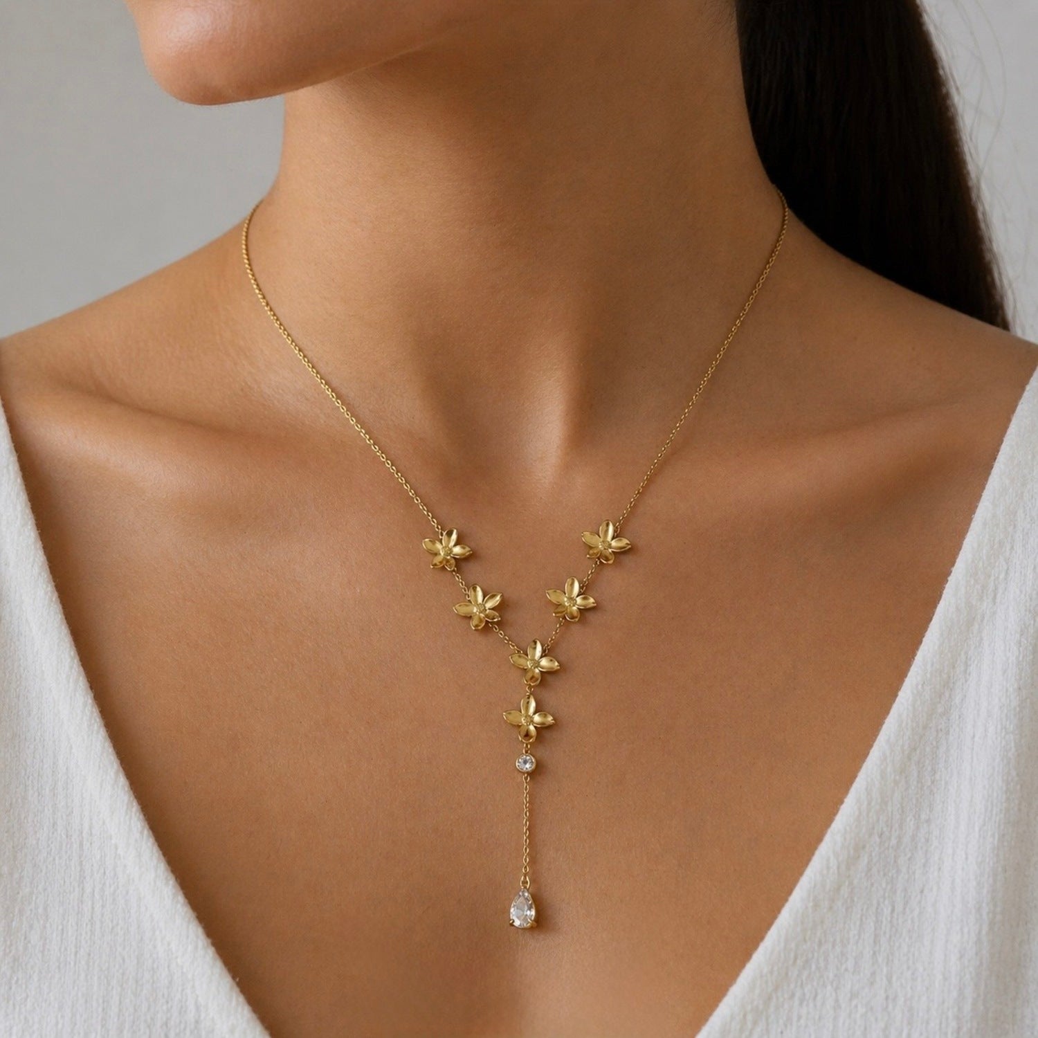 A gold-plated stainless steel chain for women in a Y-drop lariat style, featuring golden flowers and a pear-shaped crystal pendant, shown on a model