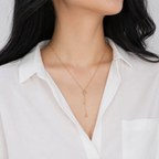 A gold-plated stainless steel Y-shaped necklace for women featuring a small crystal flower pendant and a dangling chain with gold beads, shown on a model