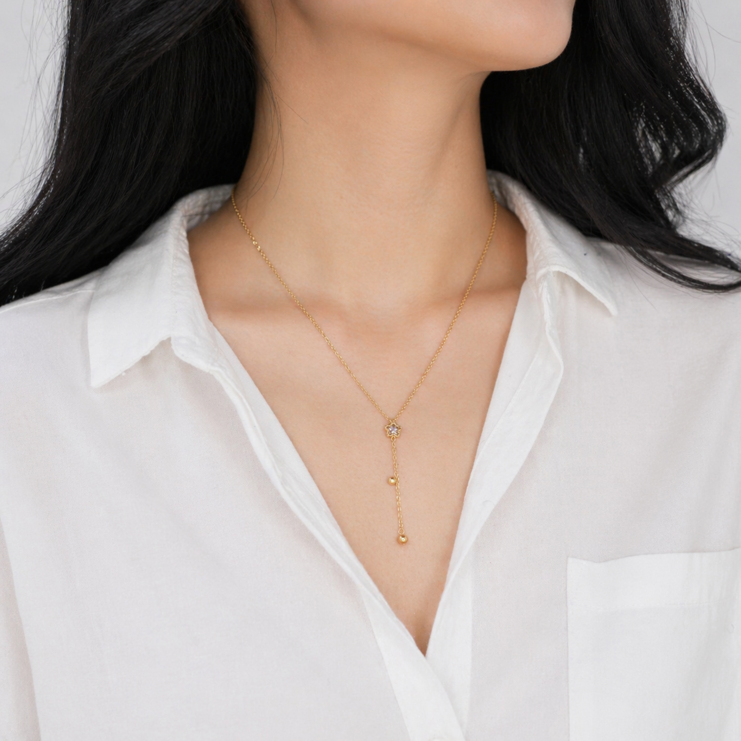A gold-plated stainless steel Y-shaped necklace for women featuring a small crystal flower pendant and a dangling chain with gold beads, shown on a model