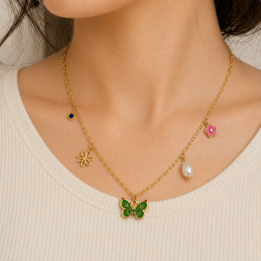 A gold-plated stainless steel chain for women featuring paperclip links and five nature-themed charms including a green butterfly, pink flower, and pearl, shown on a model