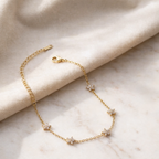 A close view of a gold-plated chain bracelet for women featuring five star-shaped floral crystal stations, shown on a cream background