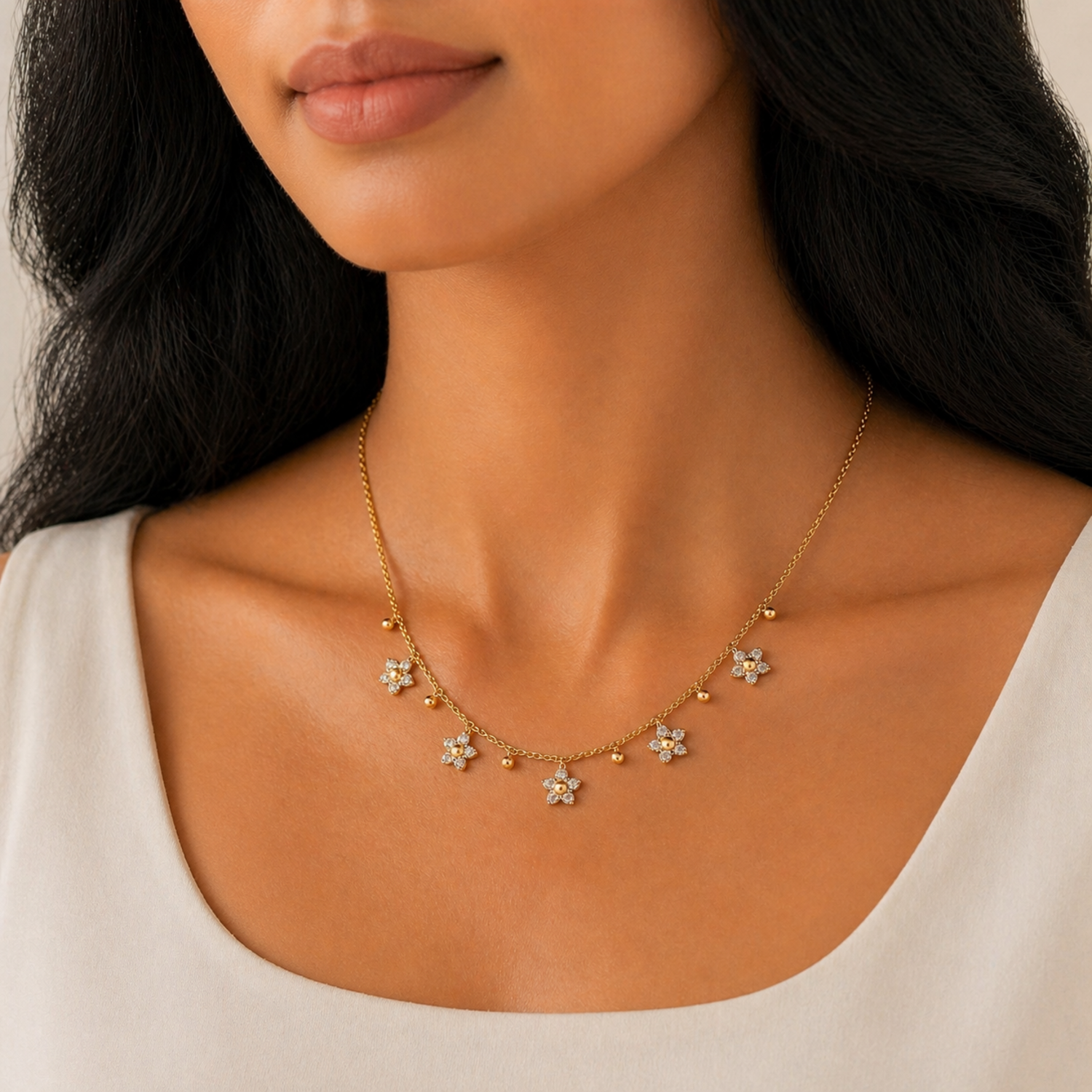 A gold-plated stainless steel chain for women featuring five crystal-encrusted flower charms and small gold beads, shown on a model