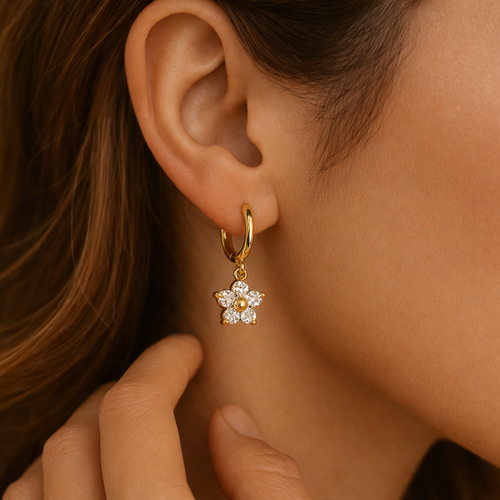 A gold-plated hoop earrings for women featuring a dangling flower-shaped charm made of clear crystals, shown on a model