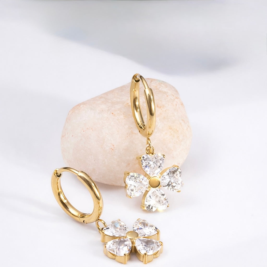 A gold-plated hoop earrings for women featuring a dangling four petal charm, shown on a textured background