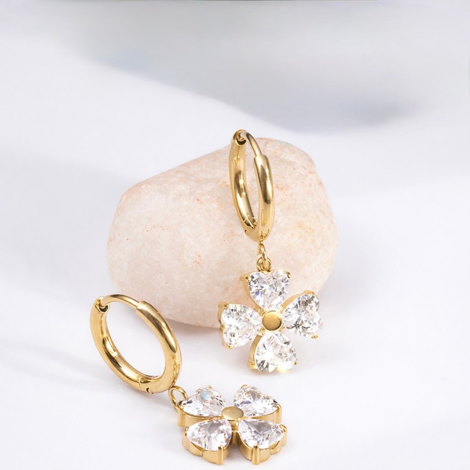 A gold-plated hoop earrings for women featuring a dangling four petal charm, shown on a textured background