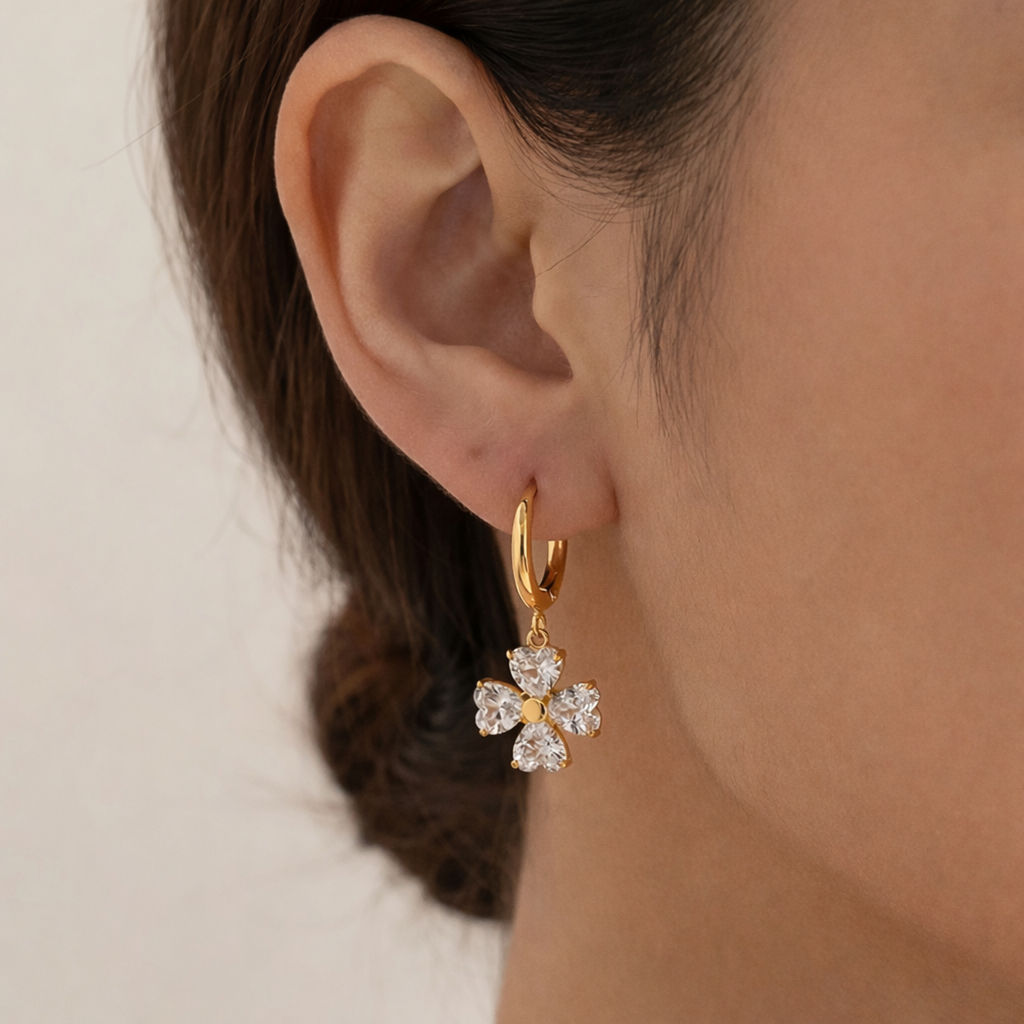A gold-plated hoop earrings for women featuring a dangling four petal charm, shown on a model