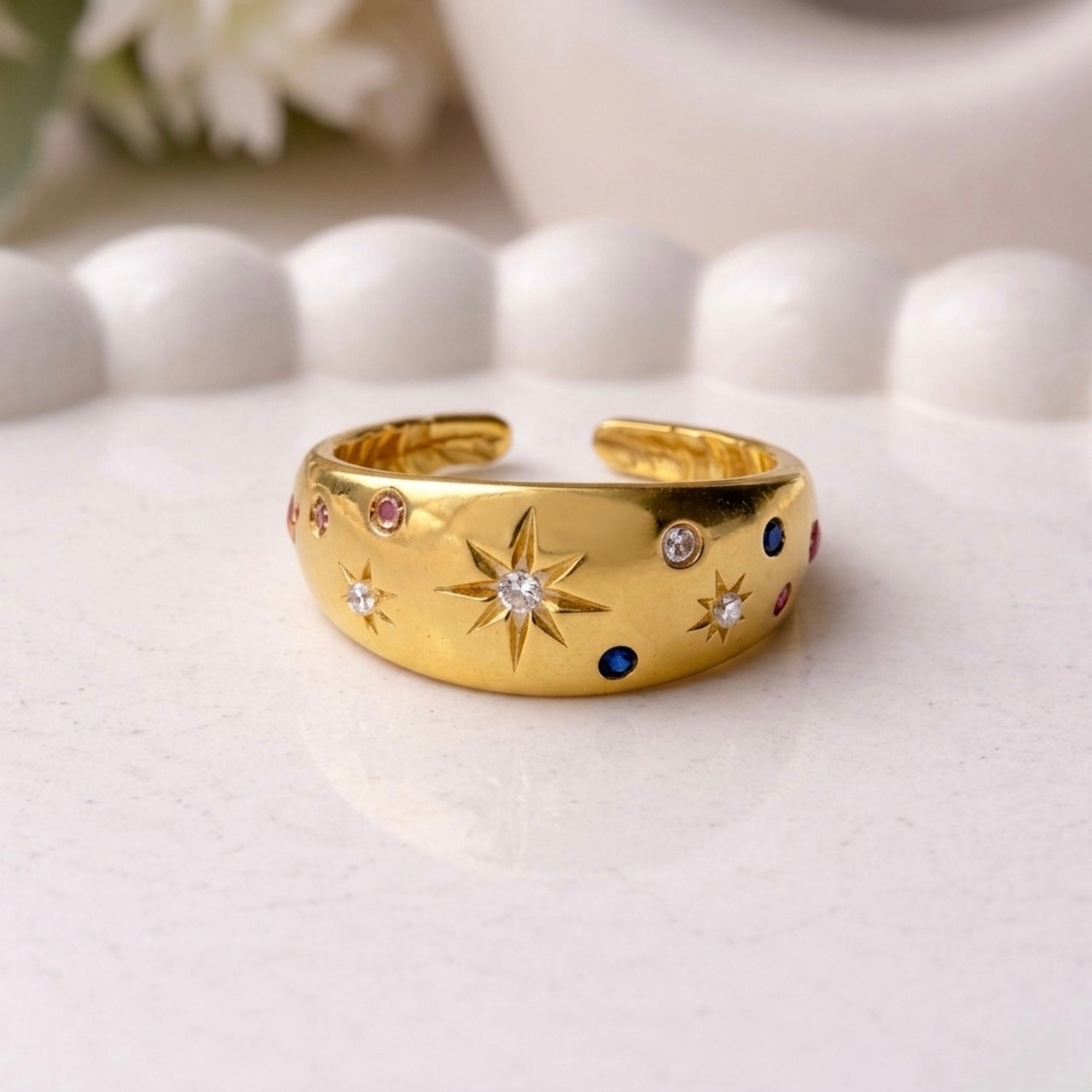 Adjustable dome ring for women featuring etched starbursts and colorful blue, pink, and clear stones on a white surface