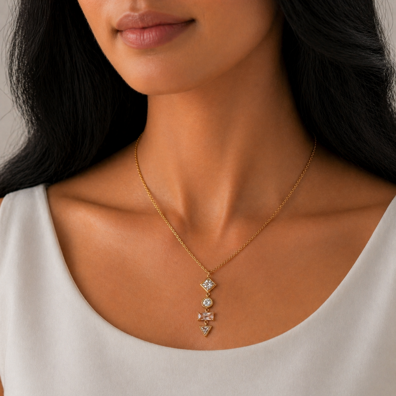 A gold-plated stainless steel chain for women featuring a vertical pendant with four different geometric crystal shapes, shown on a model