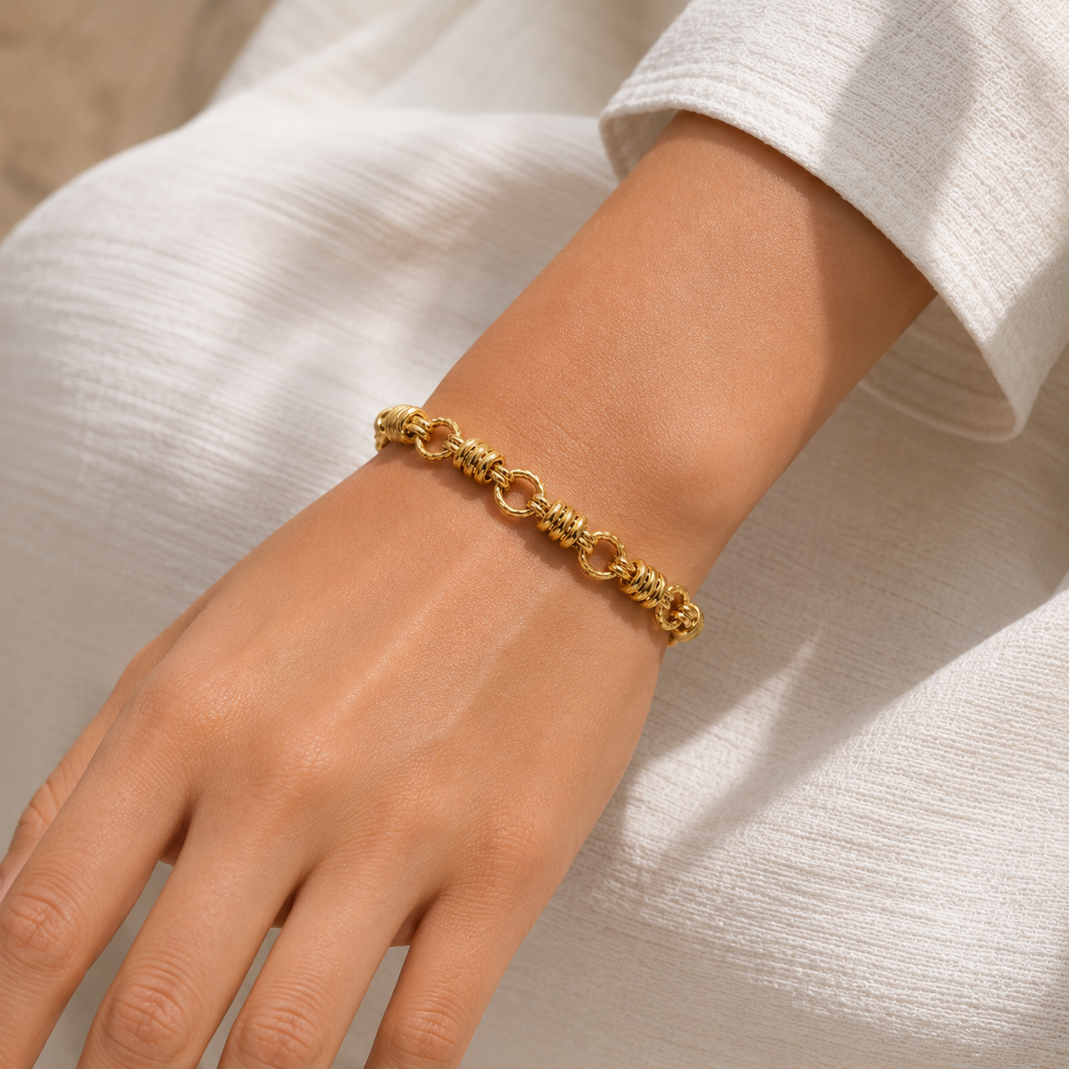 A gold-plated chain bracelet for women featuring thick polished links and textured coiled metal stations, shown on a model