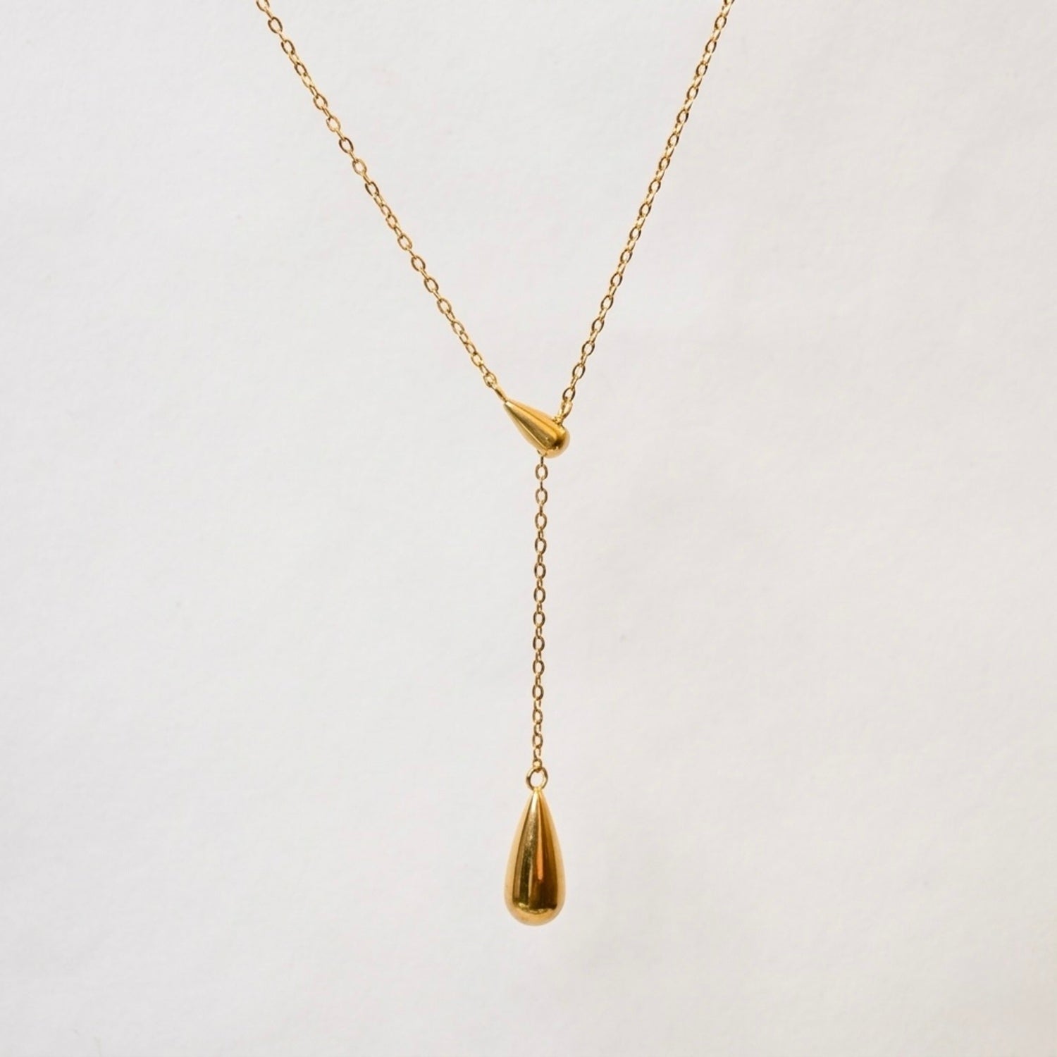 A gold-plated stainless steel chain for women featuring a Y-shaped lariat design with two polished teardrop-shaped pendants on a white textured background.