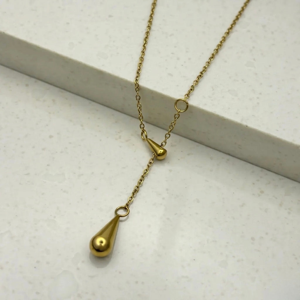 A gold-plated stainless steel chain for women featuring a Y-shaped lariat design with two polished teardrop-shaped pendants on a white textured background.