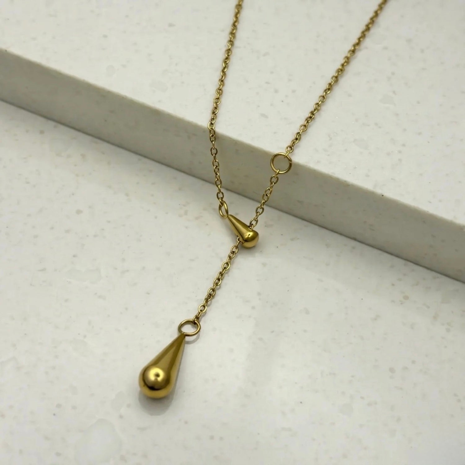 A gold-plated stainless steel chain for women featuring a Y-shaped lariat design with two polished teardrop-shaped pendants on a white textured background.
