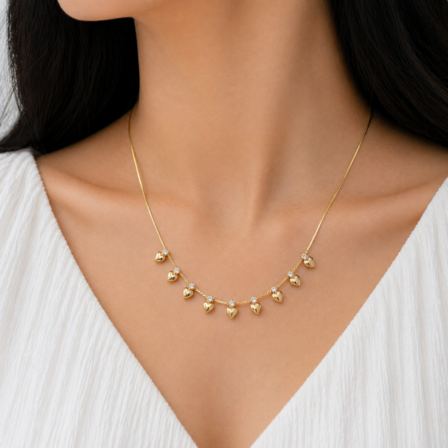 A gold-plated stainless steel chain for women featuring a fringe of nine golden hearts each accented with a small crystal, shown on a model