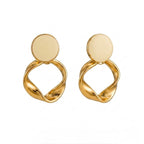 A pair of gold-plated statement earrings for women featuring a flat circular stud and a sculptural twisted hoop pendant, shown against a clean white background.