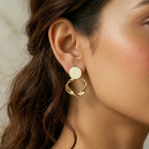 A gold-plated statement earrings for women featuring a flat circular stud and a sculptural twisted hoop pendant, shown on a model