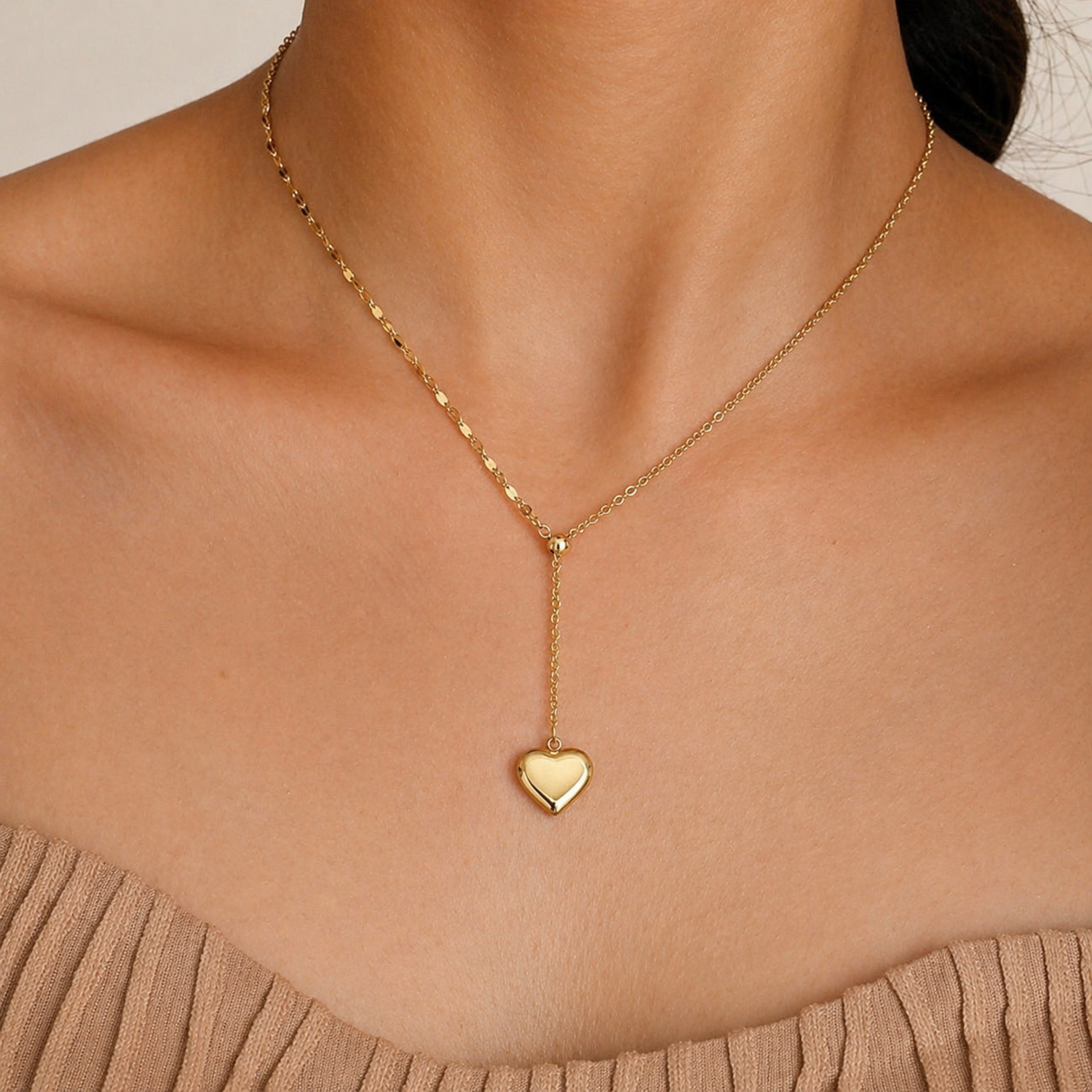 A gold-plated stainless steel chain for women featuring a Y-shaped lariat design with a polished 3D puffed heart pendant, shown on a model