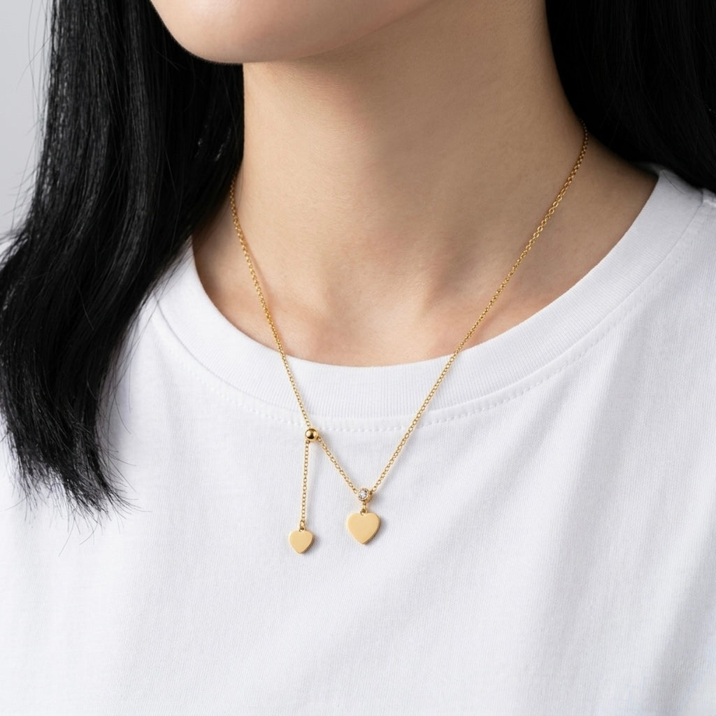 A gold-plated stainless steel chain for women featuring two heart charms and a crystal solitaire in a lariat-style drop on a model