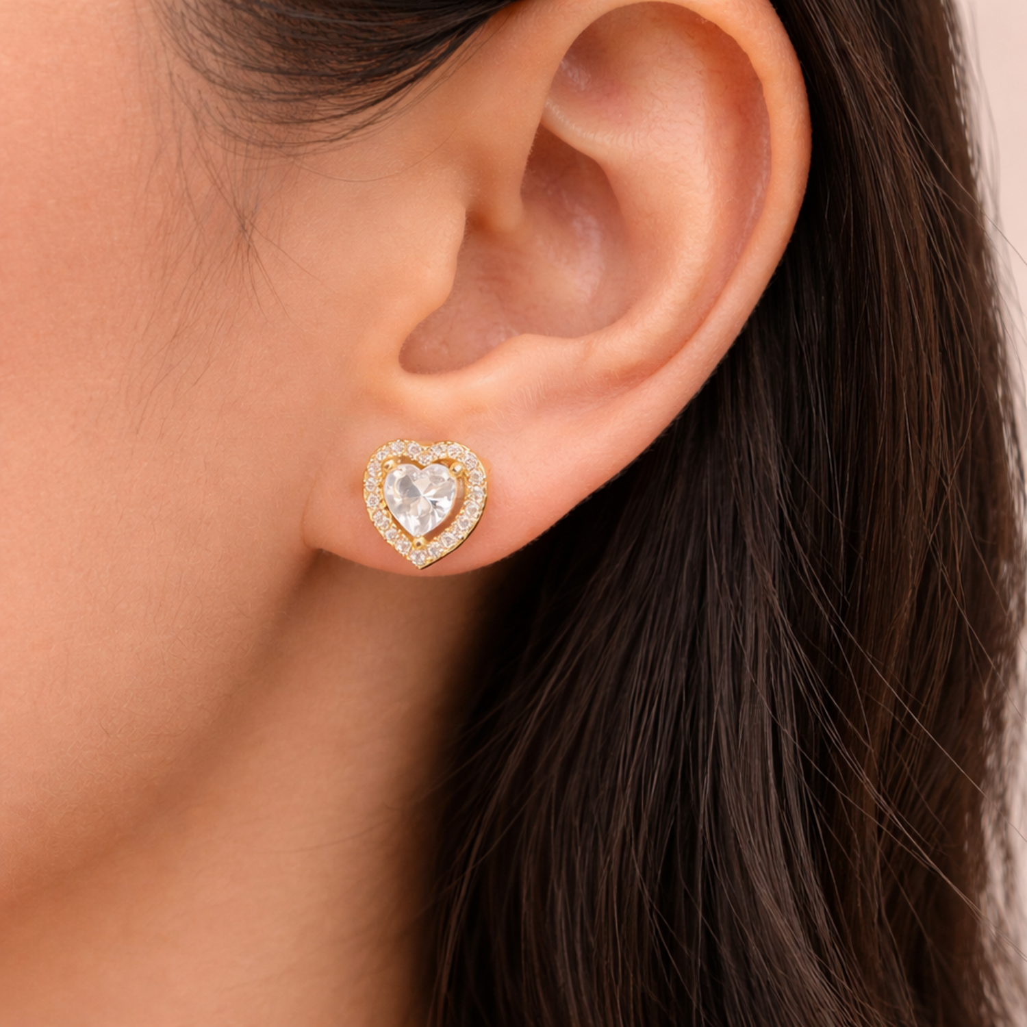 A gold-plated heart-shaped stud earrings for women featuring a large central clear crystal and a pavé halo, shown on a model