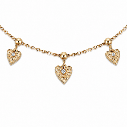 A close-view of a gold-plated ladies bracelet with a fine chain featuring three dangling filigree-engraved hearts and sparkling crystal centers.