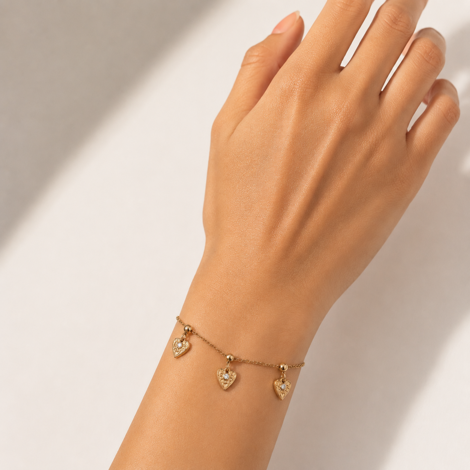 A gold-plated ladies bracelet with a fine chain featuring three dangling filigree-engraved hearts and sparkling crystal centers.
