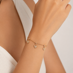 A gold-plated ladies bracelet with a fine chain featuring three dangling filigree-engraved hearts and sparkling crystal centers, shown on a model