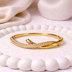 A premium gold-plated twisted hinge bangle for women featuring a continuous row of sparkling white stones on a white bobbled ceramic tray