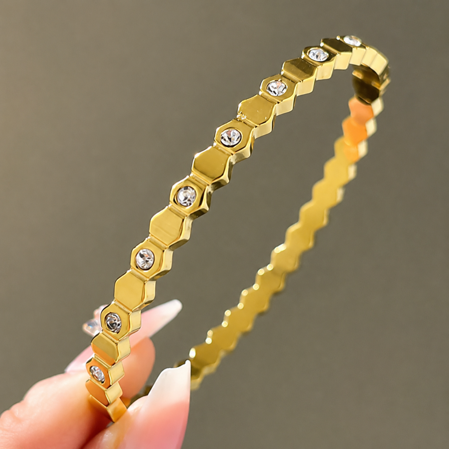 Gold bracelet with hexagonal links and embedded stones held by a hand against a neutral background
