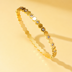 Gold bracelet with hexagonal links and embedded stones on a yellow background