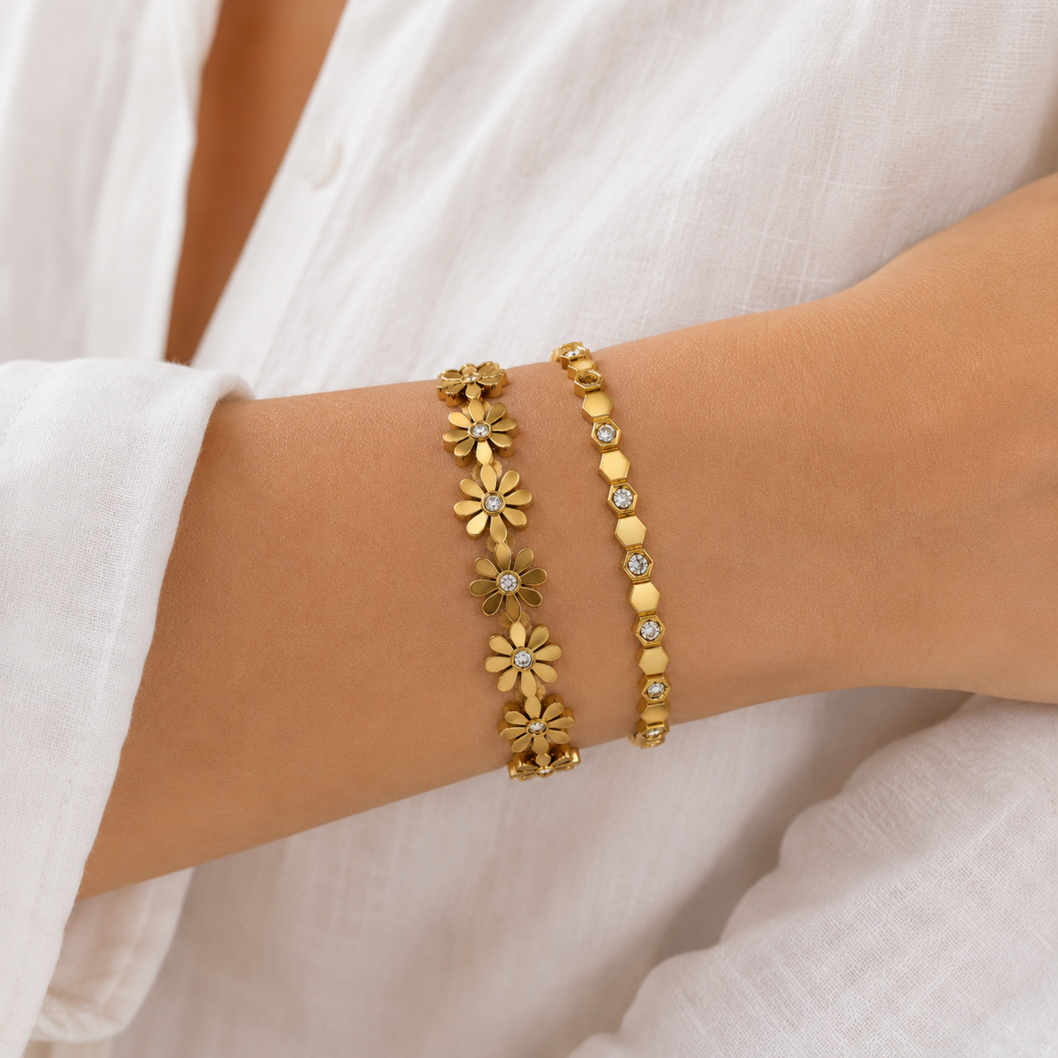 A premium two-piece gold-plated structural bracelet stack for women featuring a geometric crystal honeycomb bangle and a polished gold floral station bangle, on a model