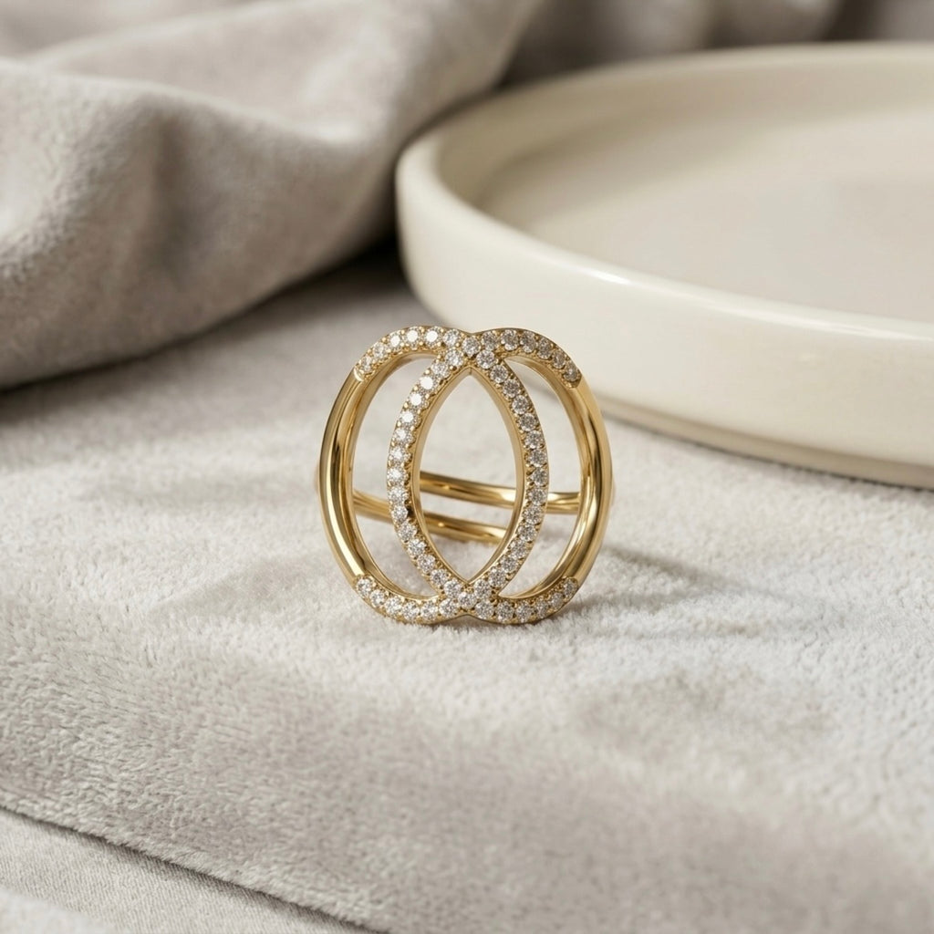 A gold plated adjustable statement ring for women featuring an interlocking oval design with pave-set white stones on a soft grey velvet surface