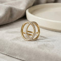 A gold plated adjustable statement ring for women featuring an interlocking oval design with pave-set white stones on a soft grey velvet surface