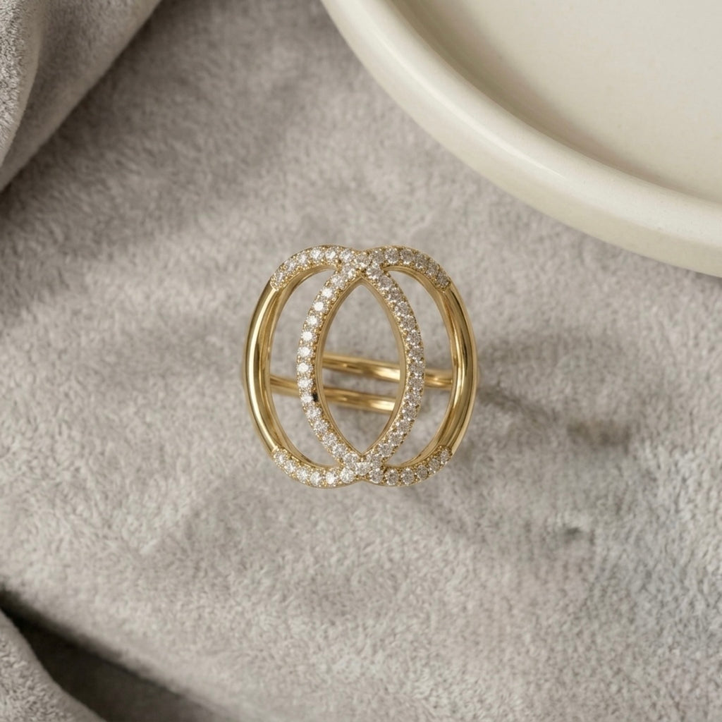 Top view of gold plated adjustable statement ring for women featuring an interlocking oval design with pave-set white stones on a soft grey velvet surface