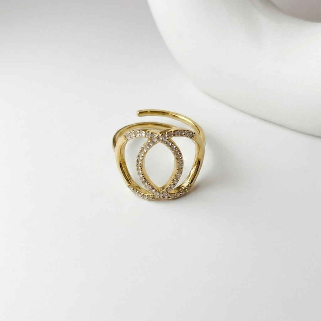 A gold plated adjustable statement ring for women featuring an interlocking oval design with pave-set white stones on a white surface