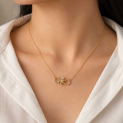 A close-up of a model wearing a delicate gold chain necklace with a small bow-shaped pendant, styled with a white collared shirt.