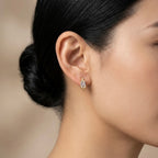 A pair of gold-plated huggie hoop earrings for women featuring a central baguette-cut clear crystal, shown on a model