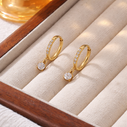 A pair of gold-plated hoop earrings for women featuring a sparkling round-cut crystal drop, shown on a jewellery organizer