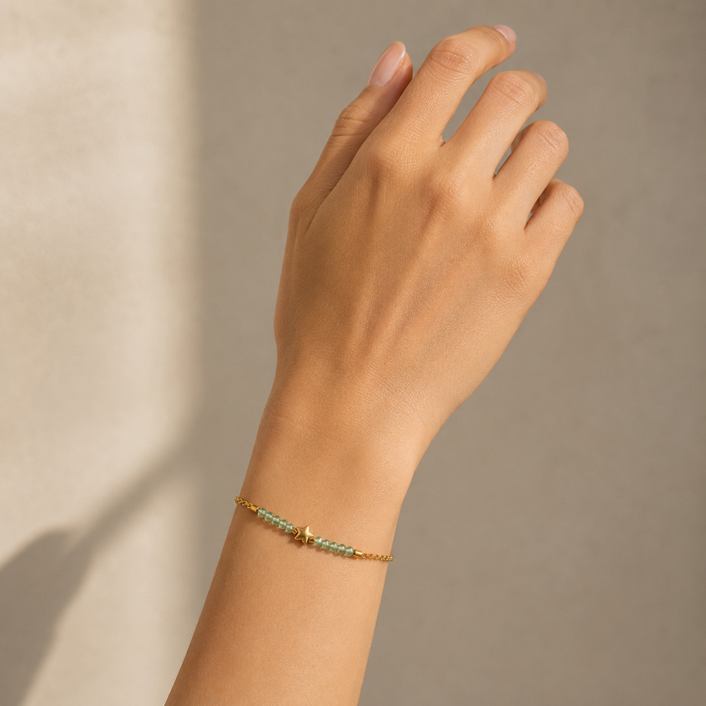 A delicate gold-plated stainless steel chain bracelet for women featuring pale-green faceted jadeite beads and a central gold star charm, shown on a model hand