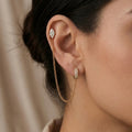 A gold-plated ear chain earrings for women connecting a crystal hoop to a marquise-cut crystal stud with a fine gold plated chain on a model