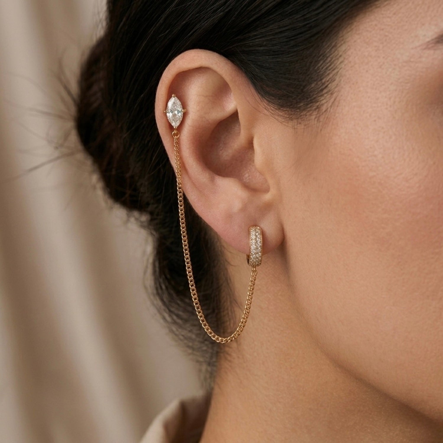 A gold-plated ear chain earrings for women connecting a crystal hoop to a marquise-cut crystal stud with a fine gold plated chain on a model