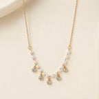 A gold-plated stainless steel chain for women featuring a curved arrangement of pearls and five dangling bezel-set crystal charms
